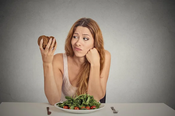 Женщина, решающая, съесть ли здоровую еду или сладкое печенье — стоковое фото